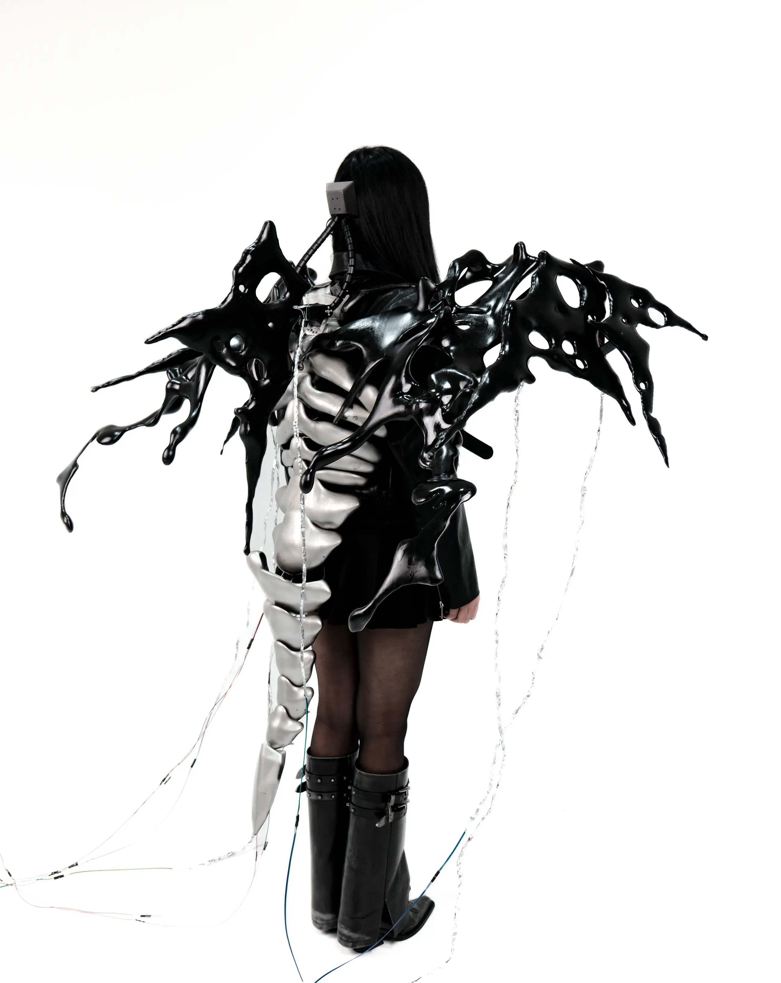 AetherWings worn full-length — wing shells at the shoulders, segmented spine down the back, wiring trailing to the floor