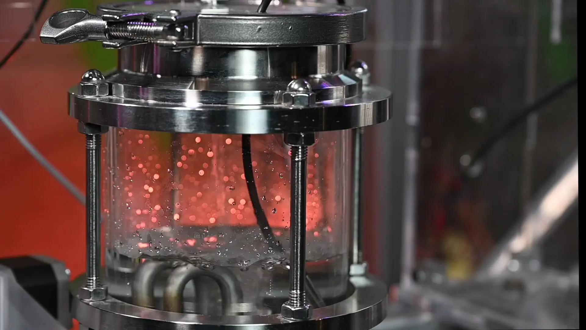 Heated water rising in the steel-and-glass chamber, lit red mid-brew