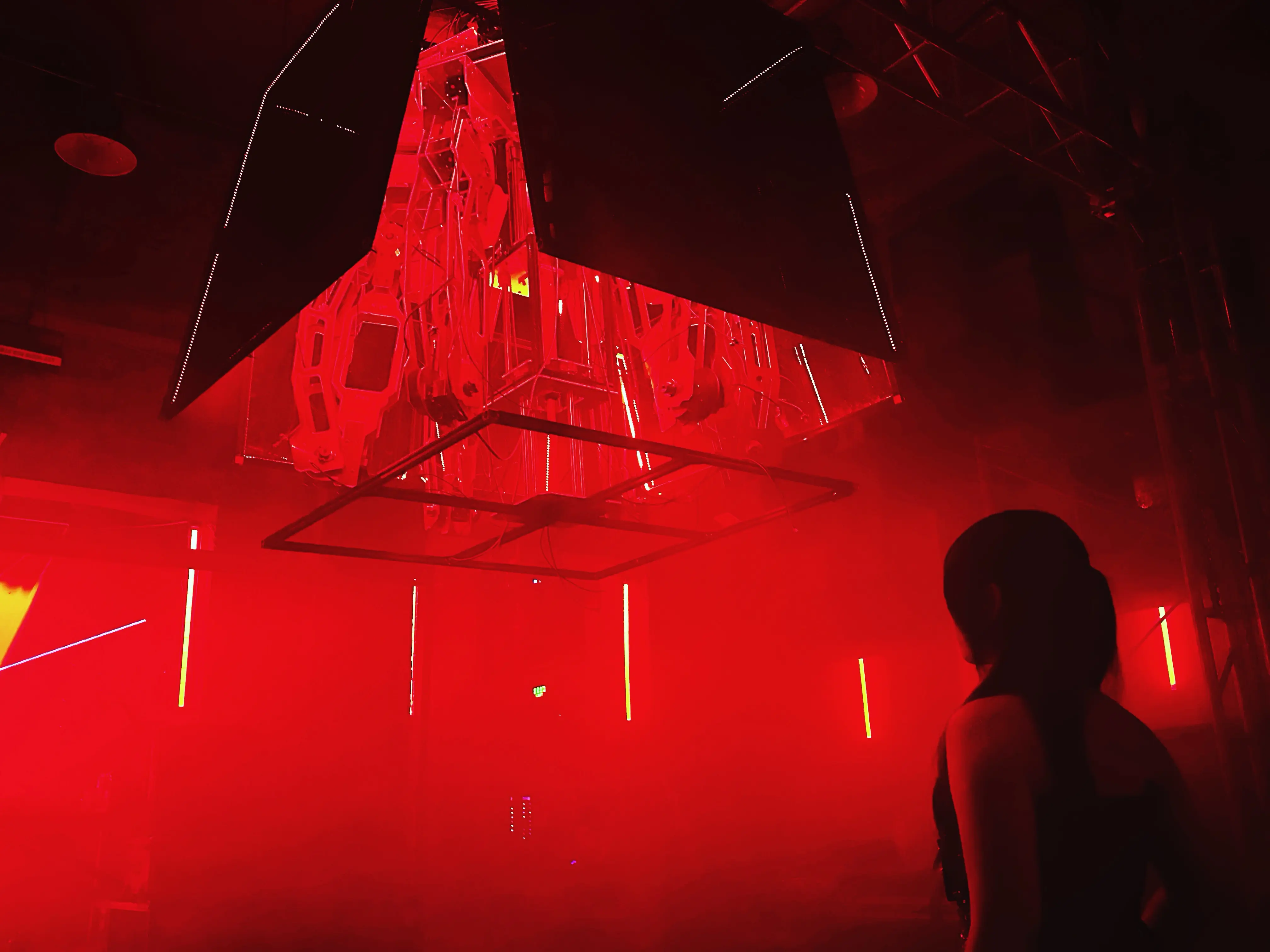 Blackbox suspended kinetic installation glowing red above an observer in fog