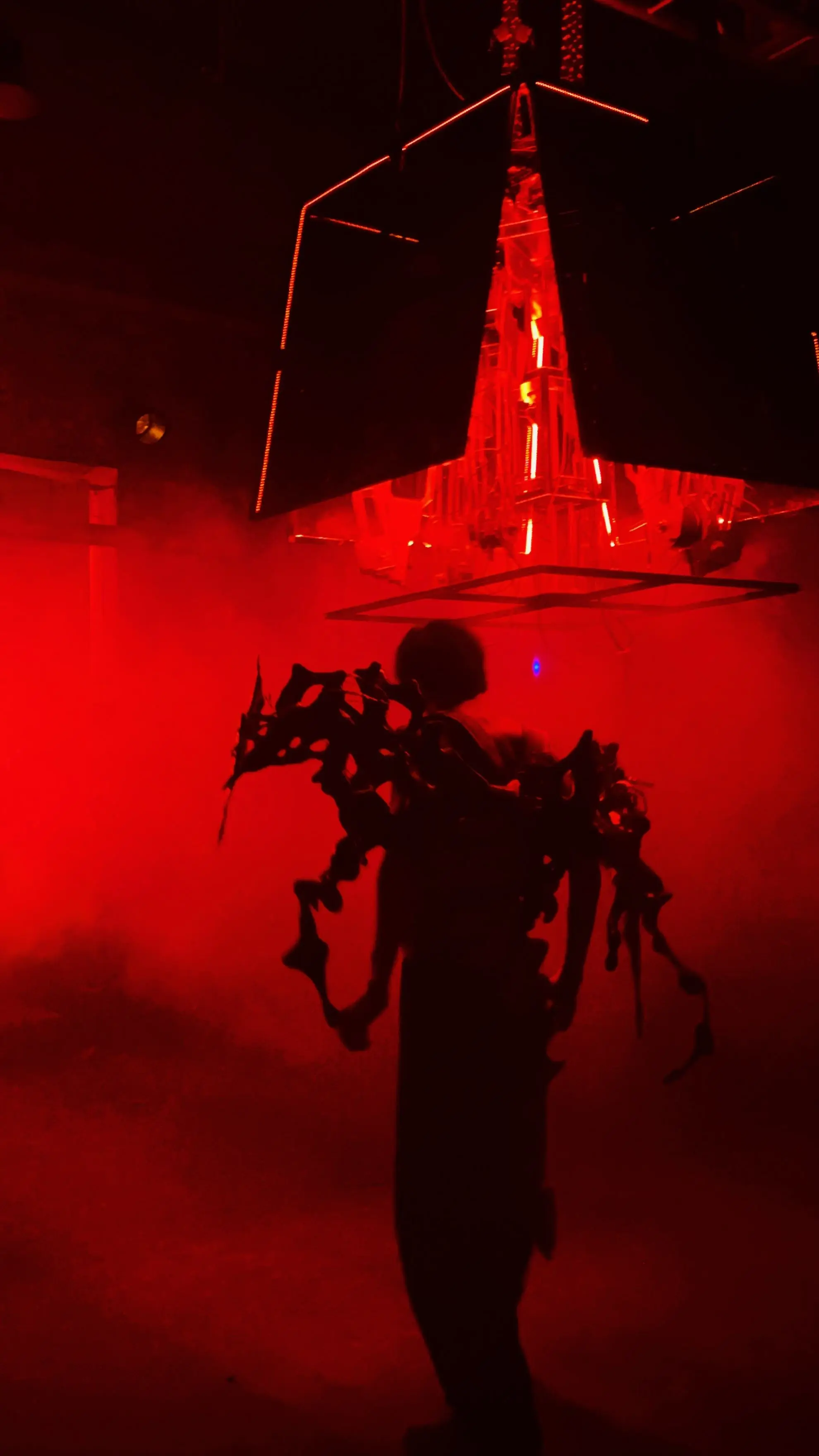 Performer wearing the mechanical extension of Blackbox in red fog